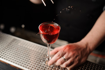 Bartender adds cherry in an alcohol cocktail