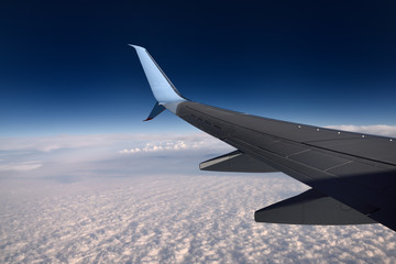 Jet aircraft wing flying above clouds with blue sky