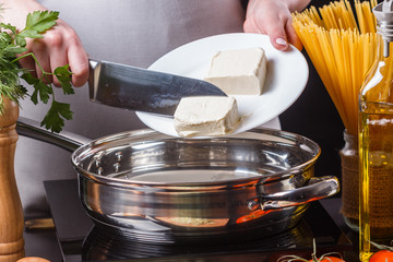 young woman in a gray apron puts butter in a frying pan