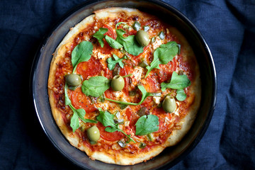 Homemade vegetarian pizza with tomato sauce, two types of cheese, tomatoes, peppers, arugula, olives and herbs. Top view.