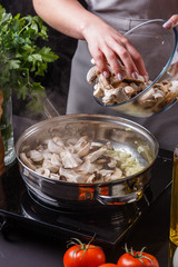young woman in a gray apron roasts mushrooms in a frying pan