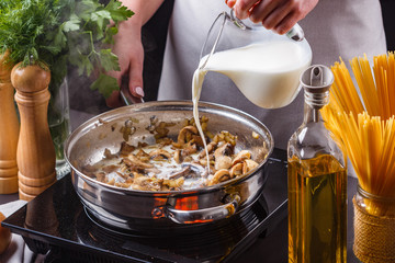 young woman in a gray apron adds milk to mushroom sauce