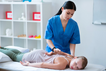 Peaceful focused lady with tied hair moving hands of lying girl