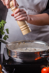 young woman in a gray apron seasoning mushroom sauce