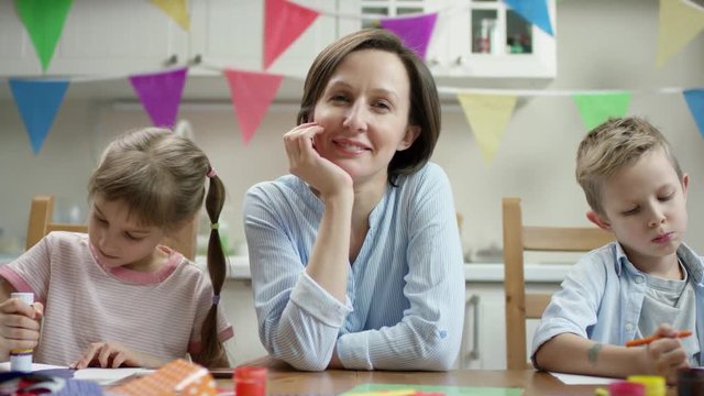 mother sitting with children while they make craft for holidays and smiling