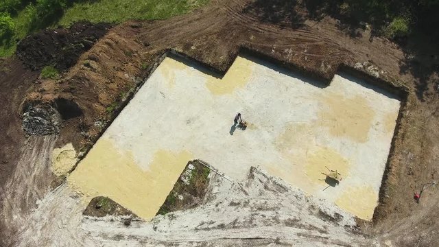 aerial of man ramming surface with vibratory plate compactor in foundation pit