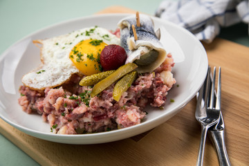 Norddeutscher Hamburger Labskaus mit Rindfleisch Corned Beef, Rote Beete, Kartoffeln, Saure Gurken, Spiegelei und Rollmops auf Teller