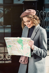 Cute young beautiful curly smiling caucasian travelling woman reading a map.