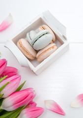 Pink tulips and macaron cookies in the basket on white background.