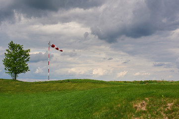 Windsock blown by the wind with overcast sky, lonely tree and green lawn
