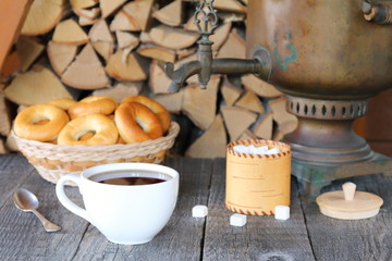 A cup of black tea from samovar on the wooden table against the background of a pile of birch firewood.