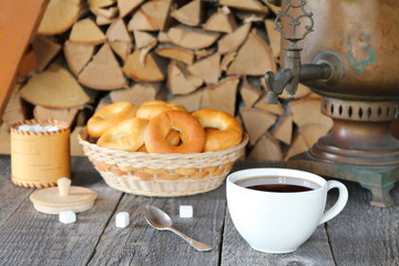 A cup of black tea from samovar on the wooden table against the background of a pile of birch firewood.