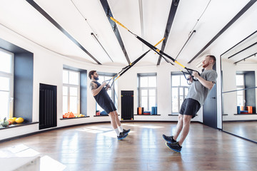 Fototapeta na wymiar Two strong male athletes are engaged in the hall with to the trx system. Concept of team spirit and the trend of a healthy lifestyle