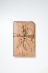 A gift wrapped in craft paper and decorated with flowers on a light background with copy space. Flat lay