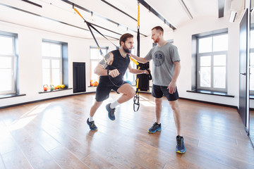 Obraz premium Male trainer teaches his student how to workout with suspended training system. Concept of strength training and work with the support of a coach