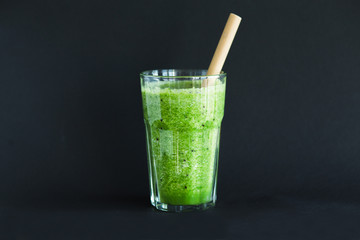 Healthy green smoothie in a glass cup on a black background