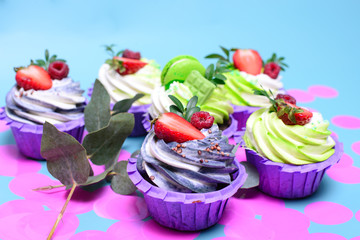 cupcakes with whipped cream decorated chocolate bar, strawberry ,macaroons on blue background. Picture for a menu or a confectionery catalog. with space for text. decorated with pink confetti.