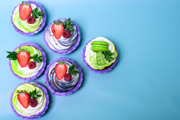 cupcakes with whipped cream decorated chocolate bar, strawberry ,macaroons on blue background. Picture for a menu or a confectionery catalog. with space for text.