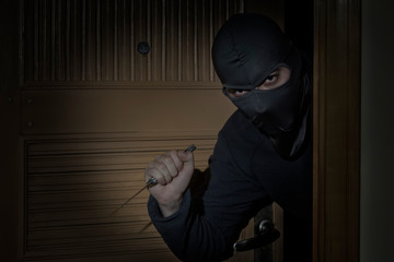Thief with a knife in his hand and a hat with a slit for the eyes sneaks into the house through the...