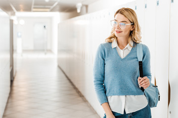 smiling student in glasses with backpack in corridor in college