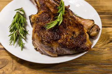 Roasted beef rib eye steak on bone with rosemary in white plate on wooden table