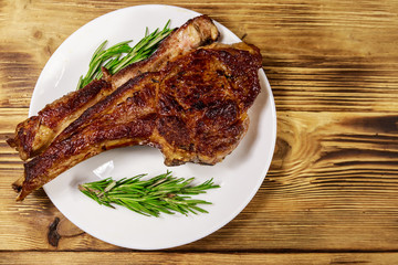 Roasted beef rib eye steak on bone with rosemary in white plate on wooden table