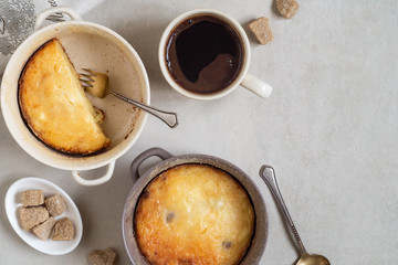 Two pans with cottage cheese casserole and cup of coffee on gray table
