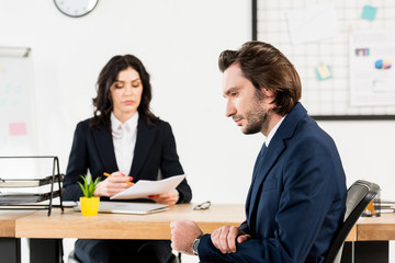 selective focus of handsome man sitting near attractive recruiter in office