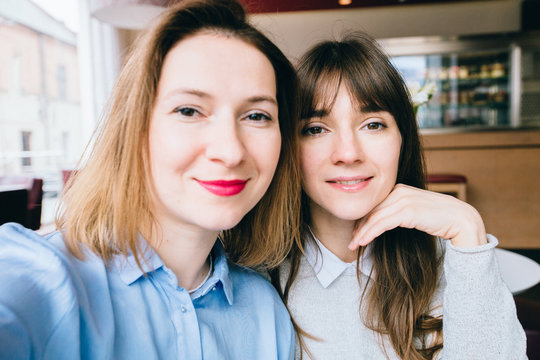 Two joyful attractive girls taking a selfie while sitting together at cafe looking at camera indoors. Adult middle age woman making selfie during lunch with sister.