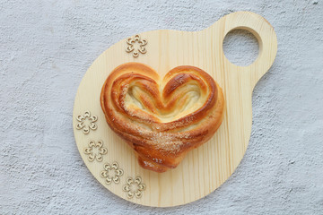 Heart Bun on a round wooden cutting board on a grey background, top view, horizontal