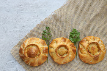 Three traditional russian chicken pies called kurnik on a table napkin laying on a grey background, top view, horizontal © Lyudmila