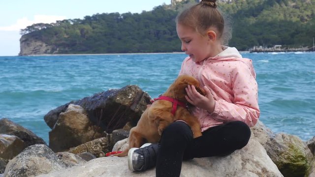 Little girl sitting on the rocks with her sweet puppy