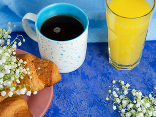 A Cup of coffee, a glass of orange and a croissant for Breakfast. Bouquet of Lily of the valley