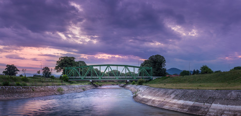 Dramatic sunset sky over old metallic railroad bridge in Pirot, Serbia, passing over silky, motion...