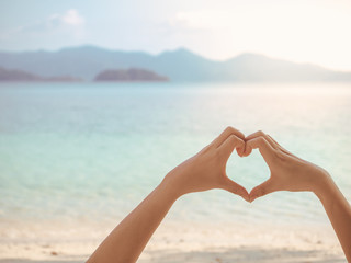 Female hands in shape heart on tropical beach with soft focus background, copy space for advertising.