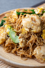 Fried dry instant noodle with chicken and chinese kale in wooden dish on concrete table.