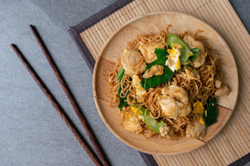 Fried dry instant noodle with chicken and chinese kale in wooden dish on concrete table.