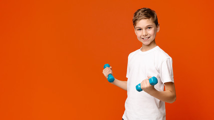 Cheerful boy exercising with dumbbells, orange background