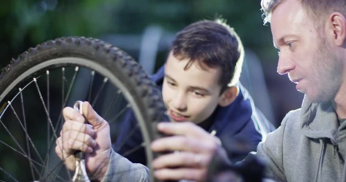 4K Dad & son spending time together & doing repairs to bicycle tyre. Slow motion.