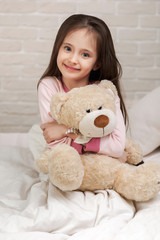adorable little child girl hugging teddy bear in bed in morning.