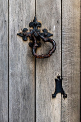 Very old wrought iron door knocker and weathered wooden door on a building in England. 