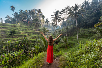 Woman with open arms in red dress on rice fields Bali in Tegallalang. Rustic Ubud village landscape outside. Fashion style - obrazy, fototapety, plakaty