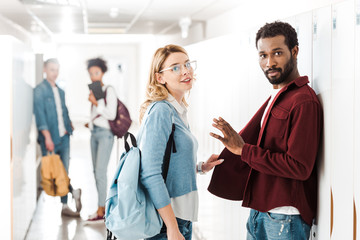 smiling multiethnic students standing in corridor in college