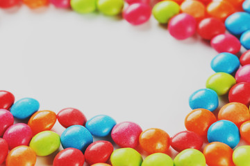 Frame of multi-colored candies close up. Rainbow colored dragee multicolored glaze on a white background