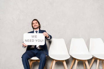 happy recruiter sitting on chair and holding speech bubble with we need you lettering