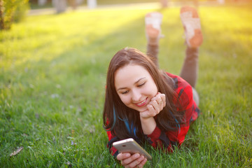 Portrait of a smiling woman lying on green grass and using smartphone outdoors