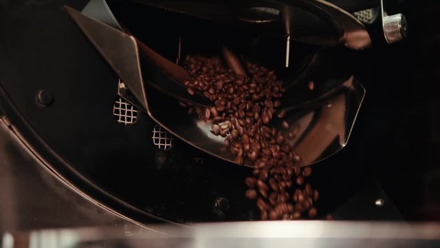 Roasted coffee beans are pouring from a metal container.