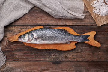 fresh whole sea bass fish on brown cutting board