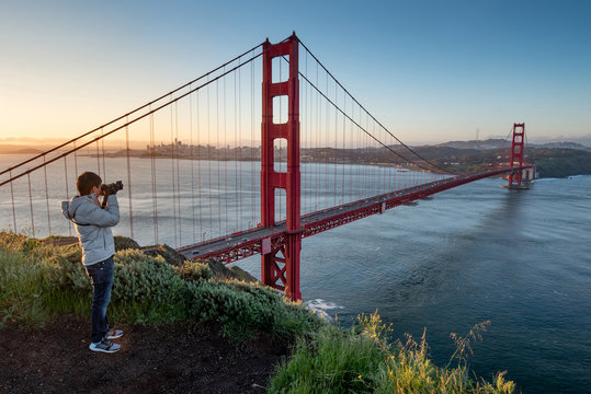 Asian man photographer and tourist enjoy taking photo of Golden Gate Bridge during sunrise, Iconic bridge and famous landmark of San Francisco, California, USA. Travel photography concept