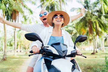 Happy smiling couple travelers riding motorbike scooter under palm trees. Tropical vacation  concept image © Soloviova Liudmyla
